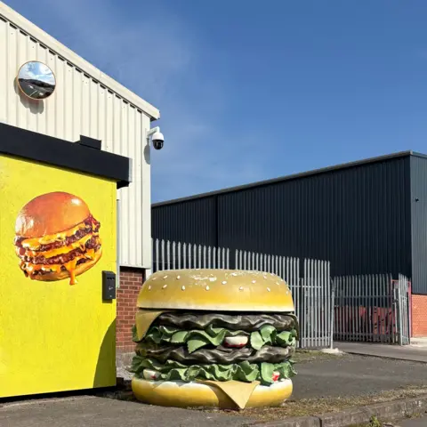 Tom Hicks A sculpture of a hamburger sits next to a white industrial unit in Cradley Heath with yellow door painted with an almost-identical hamburger 