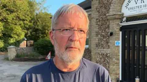 Justin North looks into the camera, he has a grey beard and is wearing glasses