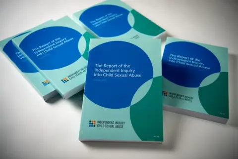 PA Media Several copies of a book, entitled: "The Report of the Independent Inquiry into Child Sexual Abuse" are arranged on a white surface. The cover is blue, green and turquoise and features an overlapping circle design.