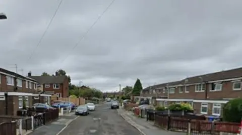 Modern terraced housing on a suburban street with parked cars.