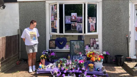 A house with a window display of photos and flowers arranged as a memorial.