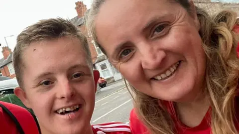 A woman and her son pose for a photo, both are smiling and wearing red. 