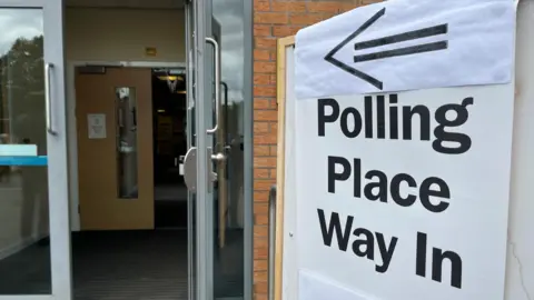 A polling place sign pointing towards an open door at a school in Hamilton