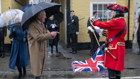 PA Media King Charles points at the town crier, who is wearing a red coat and holding the Union flag.