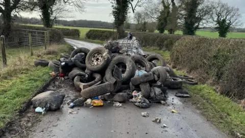 A big pile of tyres and other waste blocking a country lane