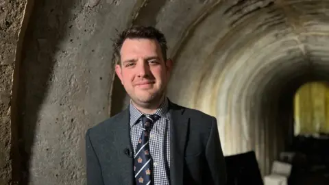 BBC/Kate Bradbrook Nigel Burgham with short dark hair wearing a grey jacket