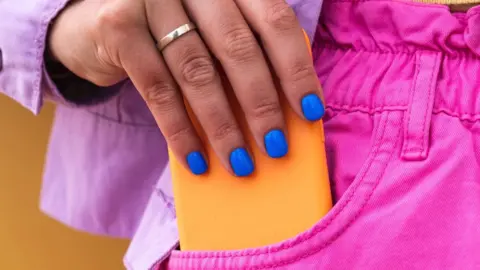 A woman takes a smartphone out of her pocket.