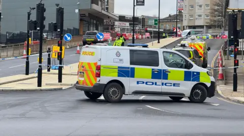 A police van and some police cats on a busy road with buildings on each side