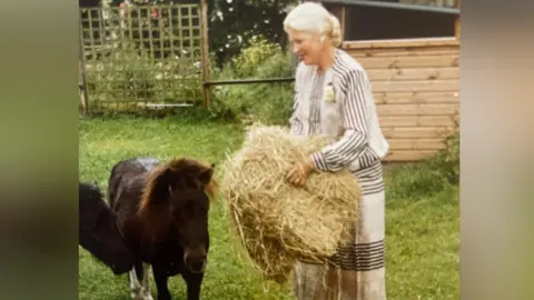 Contributed A younger Jean stands with a hay bale in her hands next to two dark brown small ponies.