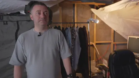 Chris Jardine, Men with a dry black hair, drawn stands in the loft and mictophone of black mictophon. Really dress, tarpolen and color can be seen in the back. He went to the left of the camera with a serious expression.