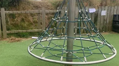 A netted cone-shaped climbing frame held up by a metal pole.