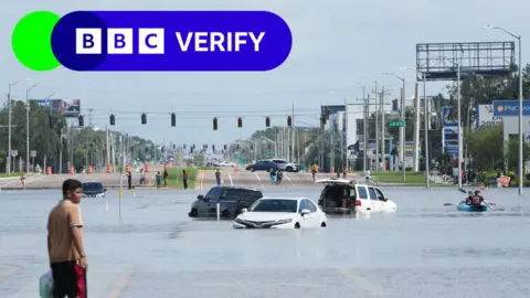 Getty Images A young man walks past vehicles flooded in the water in the streets of the Southeast Seminole Heights section of Tampa.