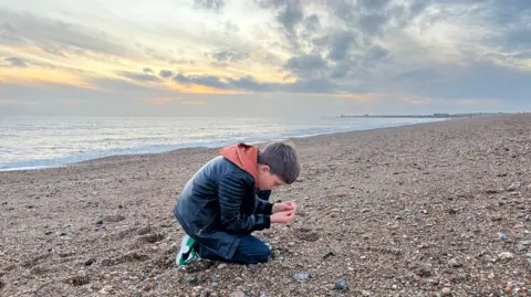 George Carden / BBC Ben kneeling on a shingle beach in Shoreham where found a Neanderthal hand axe 