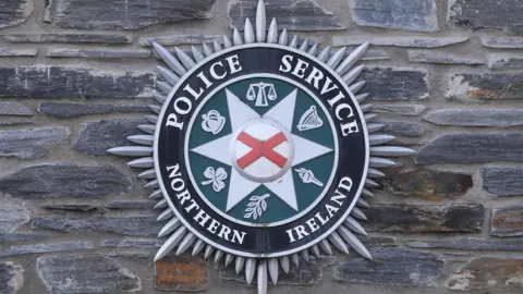 The Police Service of Northern Ireland badge pictured against a stone wall. 