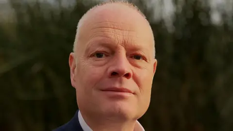 Royal Devon University Healthcare NHS Foundation Trust Sam Higginson. He is a middle-aged man with short white hair. He is clean shaven.