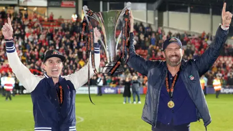 PA Media Ryan Reynolds and Rob McElhenney holding the National League Trophy on the pitch