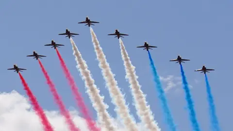  PA Nine Red Arrows planes in a V formation. The planes have red, white and blue coloured smoke.
