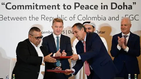 AFP via Getty Images Men in suits exchange documents during a signing ceremony.