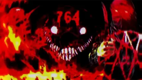 Dark and sinister-looking images on a video still - the background is black, with what look like flames in the foreground, a pentangle and possibly a monstrous face in the middle with "764" above its eyes