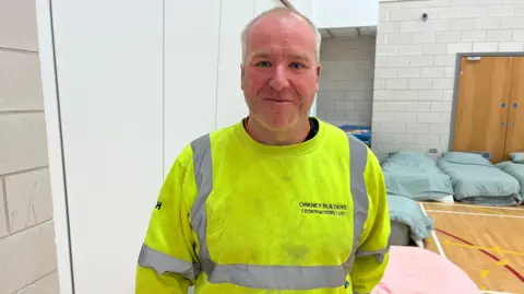 A man in a high-vis jumper, standing in front of blow up beds.