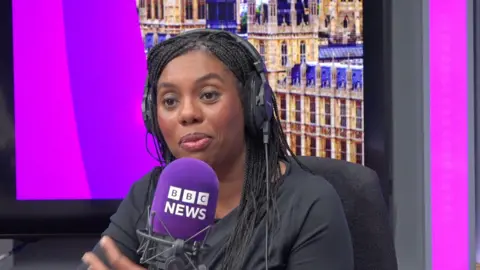 A woman sits in a purple radio studio