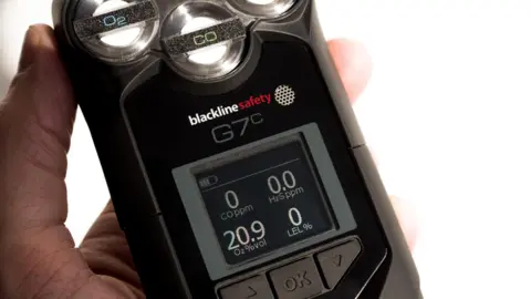 Rockall Safety The picture shows a G7c gas monitor in the palm of a hand. It is black with an LED-type screen and has silver and black buttons on it. 