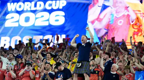 PA Media Scottish fans in a large crowd celebrate during a football game. One fan is standing high above the others wearing a kilt.
