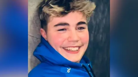 Family handout A young man with dark hair and blonde highlights. He is wearing a bright blue hooded jacket.