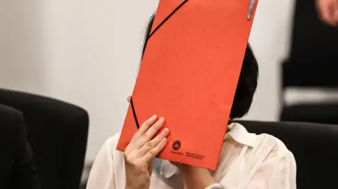 EPA/Shutterstock A woman in a white shirt holds a red folder in front of her face