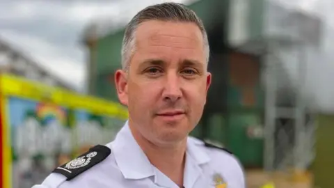 Henry Griffin, deputy chief fire officer at Suffolk Fire and Rescue Service, is wearing his fire officer uniform, which is a white shirt with epaulettes. He has short, grey hair.  