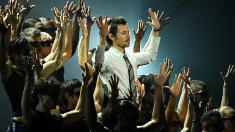 Harry Styles performs during the Brit Awards 2026 at Co-op Live, Manchester wearing a shirt and tie surrounded by back-up dancers.