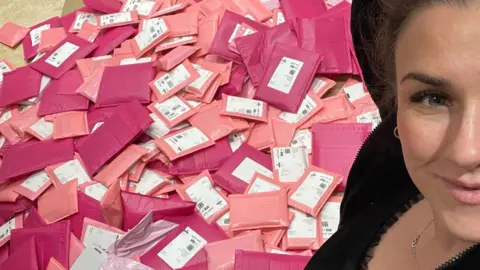 Supplied A selfie of Lucy posing next to hundreds of pink parcels.