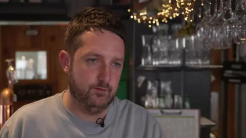 BBC/Luke Manterfield A picture of Chris Marson who has brown hair and a beard, standing at his bar in Scarborough.