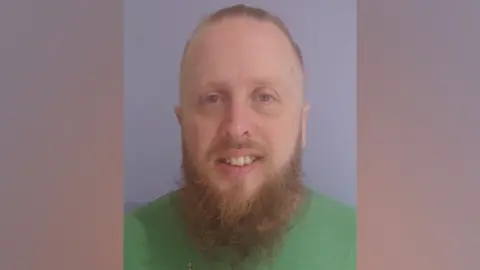 A man with red hair and beard, wearing a green t-shirt 