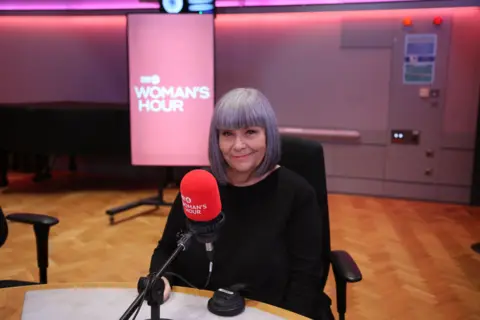 Dawn French wearing a black top, sat in a studio with a red mic in front of her.