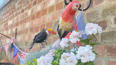 Stuart Gent Colourful bunting and two fake birds are attached to a wall. 