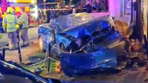 A blue car is heavily damaged after crashing into a shop