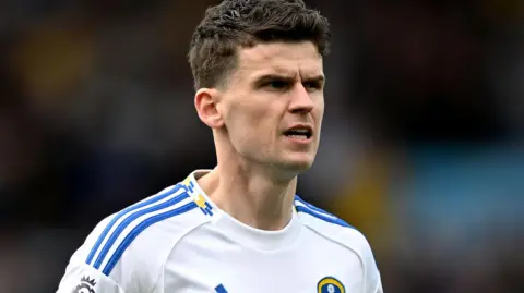 Sam Byram wearing a Leeds shirt looks to his right with a slightly open mouth