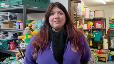 A woman with long brown hair smiling and stood in front of toys
