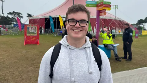 A man with glasses and a grey hoody smiles at the camera