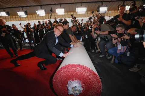 Mike Blake/Reuters Conan O'Brien, wearing glasses and a suit, pushes a immense  rotation  of reddish  carpet retired  arsenic  a large  assemblage  of photographers takes his picture