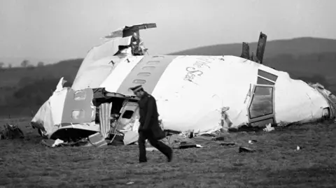 Press Association Police office walks past the wrecked nose section of Pan Am flight 103 in a field at Lockerbie after the plane was blown apart by a terrorist bomb. 