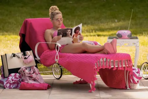 Jessica Brooks/Prime Video A woman in a pink bikini lies on a deck chair covered in pink blankets, reads a magazine. there are pink towels, a tote bag and a radio next to her.