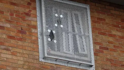 HMIP A damaged prison window with holes in the wire mesh covering the perimeter.