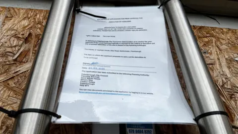 Emma Baugh/BBC A laminated notice attached to the door of a former nightclub door showing how it is required for demolition.