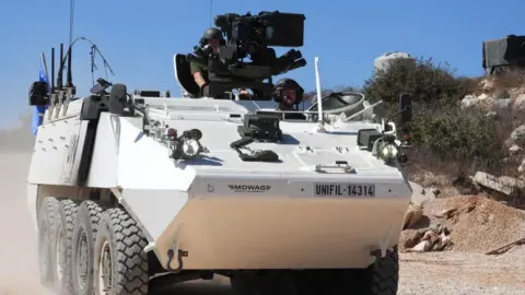 Two Irish peacekeepers driving a white tank down a sandy road in Lebanon