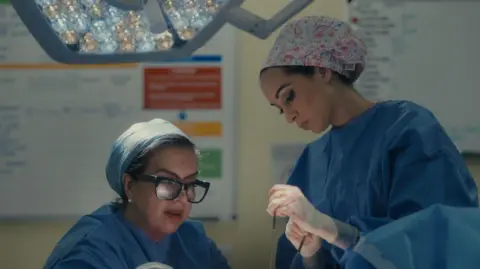 Channel 5 Two women in blue scrubs focusing on their patient while holding surgical tools