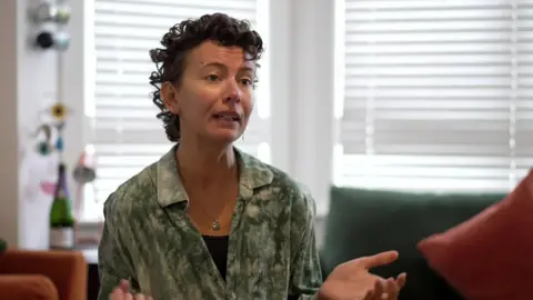 Woman with short brown curly hair wearing a green shirt.