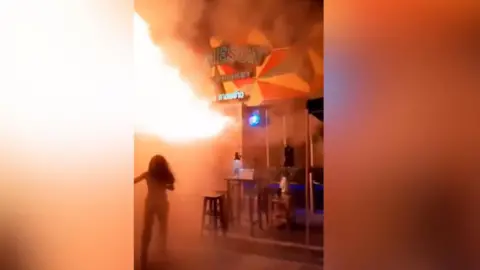 A woman flees flames bursting from a bar's entrance
