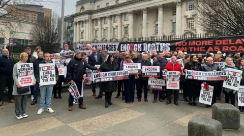 A group of road campaigners outside the High Court in Belfast. They are holding up signs and banners saying enough is enough.